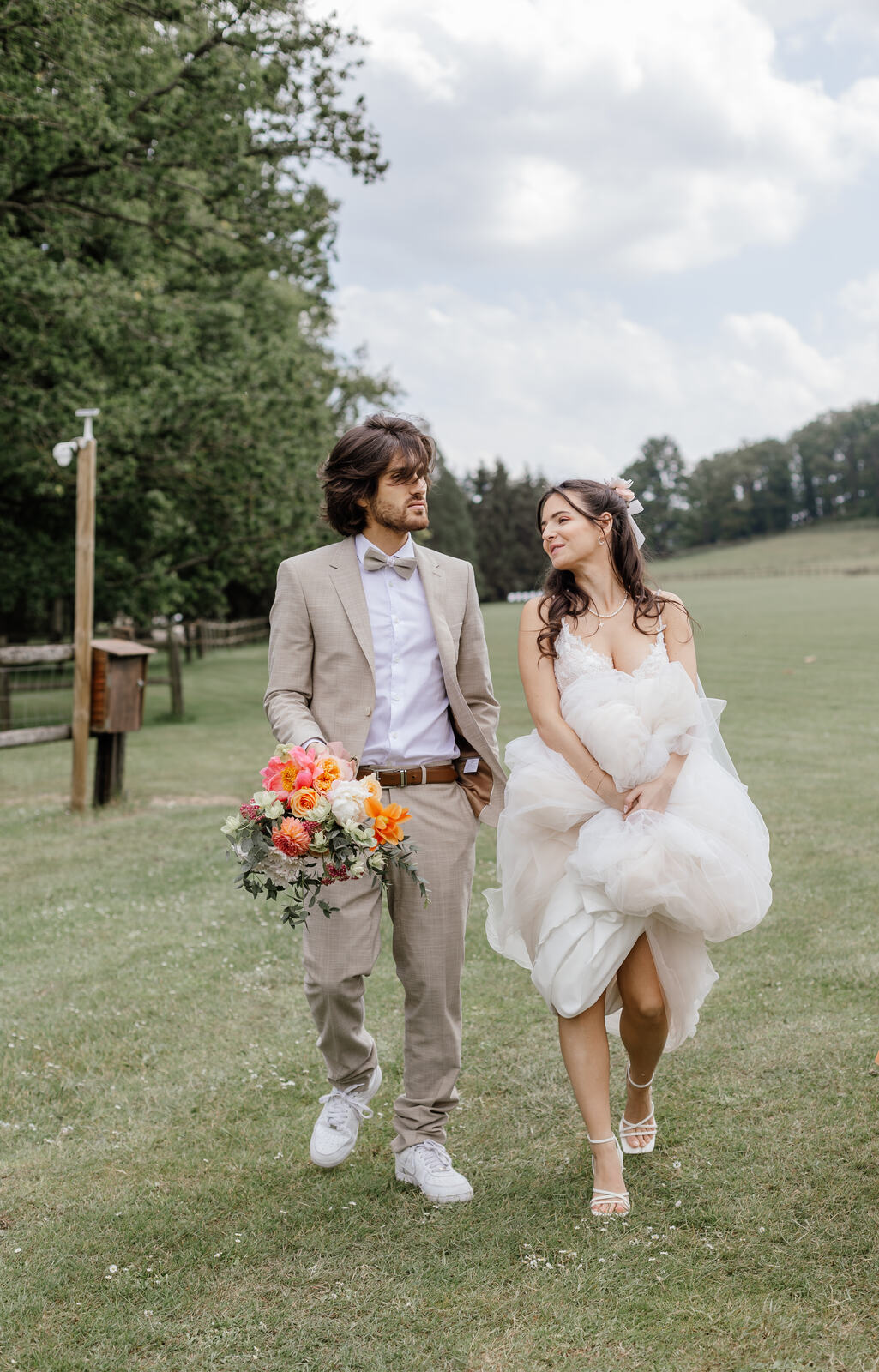 Mariés riant en courant dans un pré, un bouquet multicolore à la main