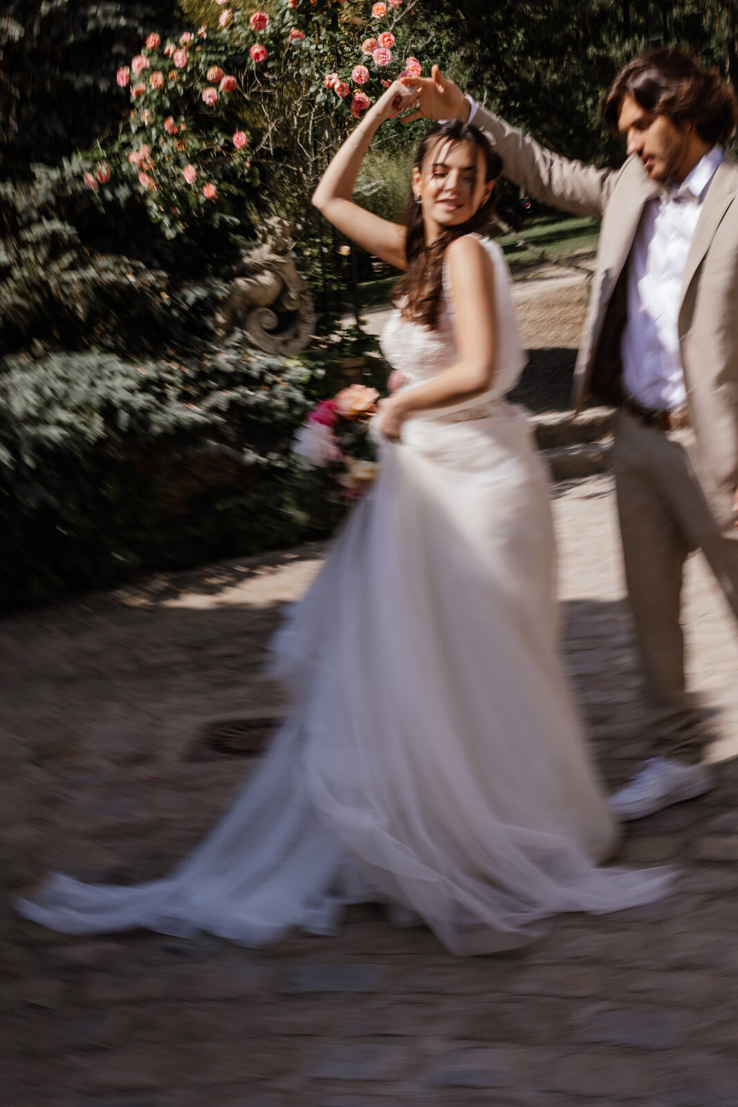 Mariée éclatant de rire sous une allée de rosiers grimpants, moment complice avec son époux
