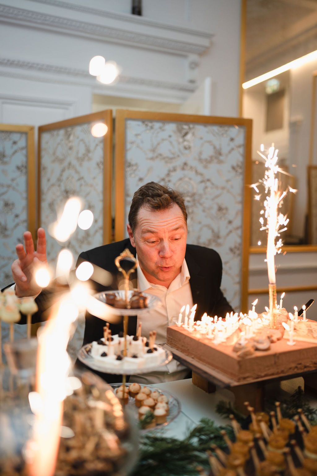 Homme soufflant les bougies d'un gâteau scintillant lors d'une fête d'anniversaire