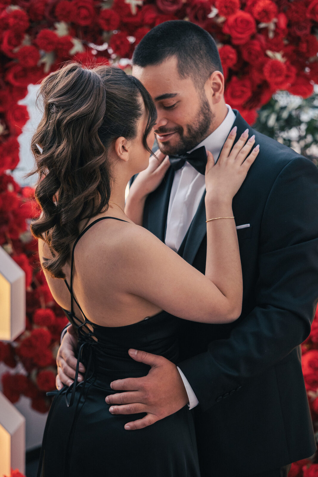 Couple enlacé tendrement devant un mur de roses rouges après la demande en mariage